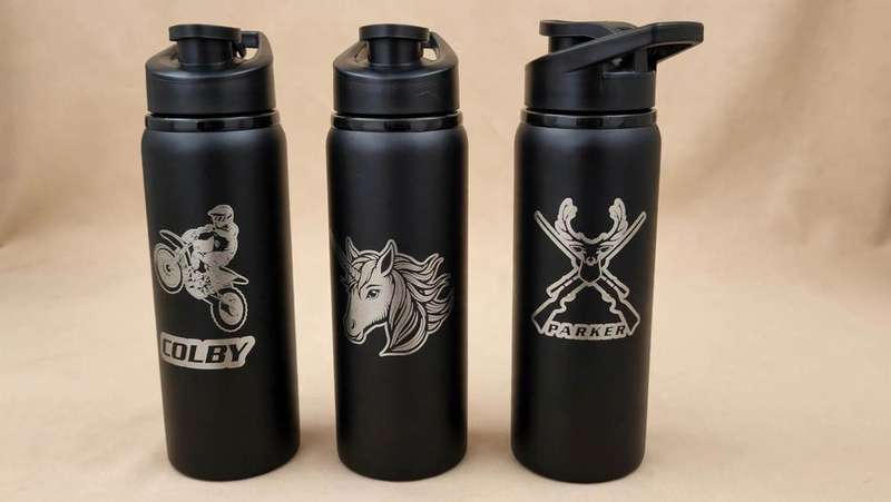 Three black water bottles etched with dirt bike, unicorn, and deer designs